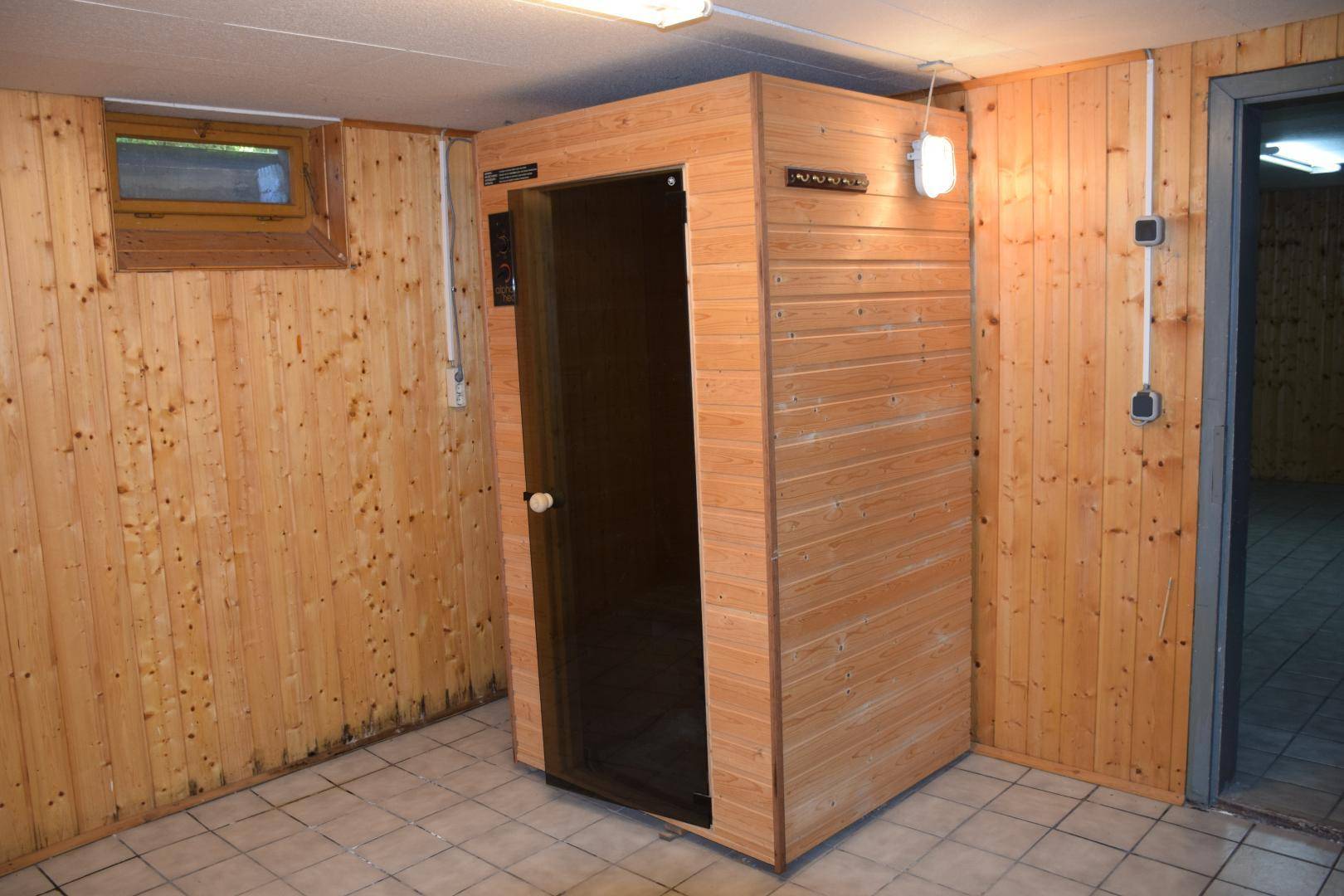 Kellerraum mit Holzvertäfelung, Fliesenboden und einer eingebauten Sauna für Wellness.