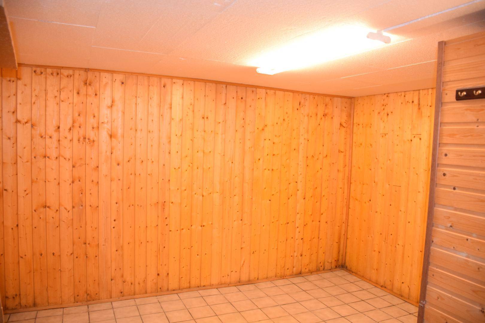 Raum im Kellergeschoss mit Holzvertäfelung an den Wänden und Fliesenboden.