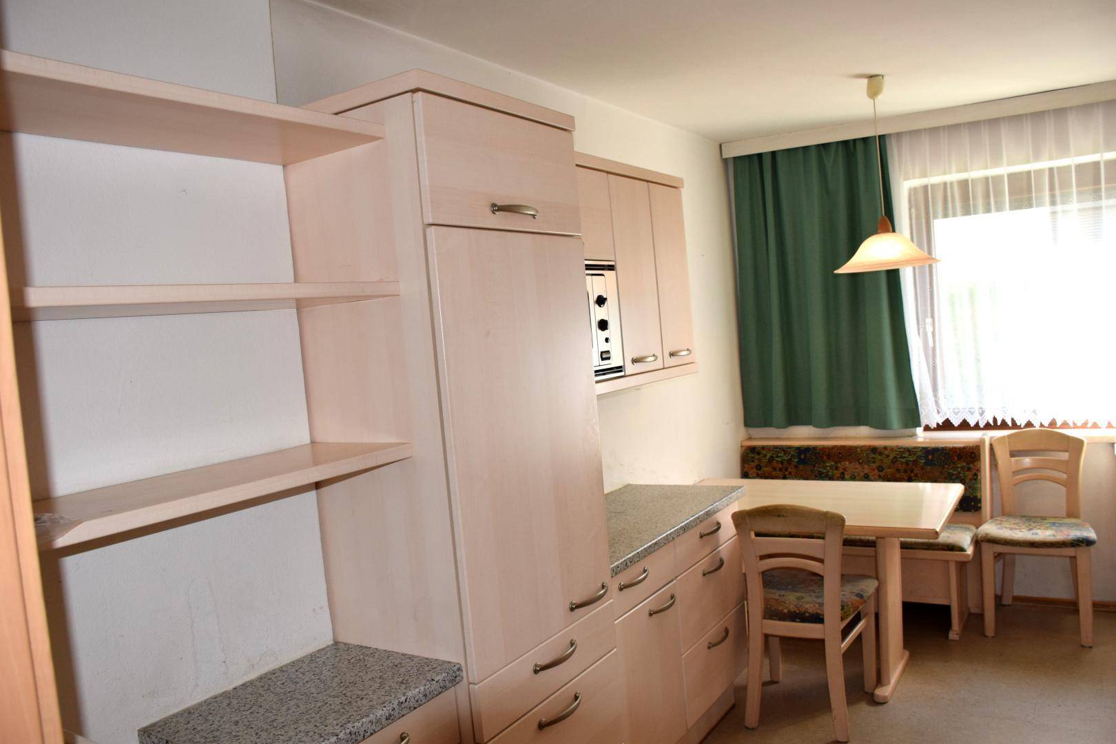 Weitere Ansicht der Wohnküche mit Einbauschränken, Mikrowelle und Essbereich am Fenster.