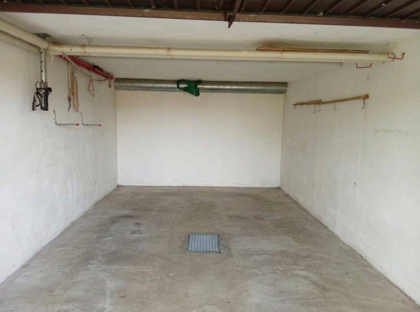 Leere Garage mit Betonboden und sichtbaren Leitungen an der Decke.
