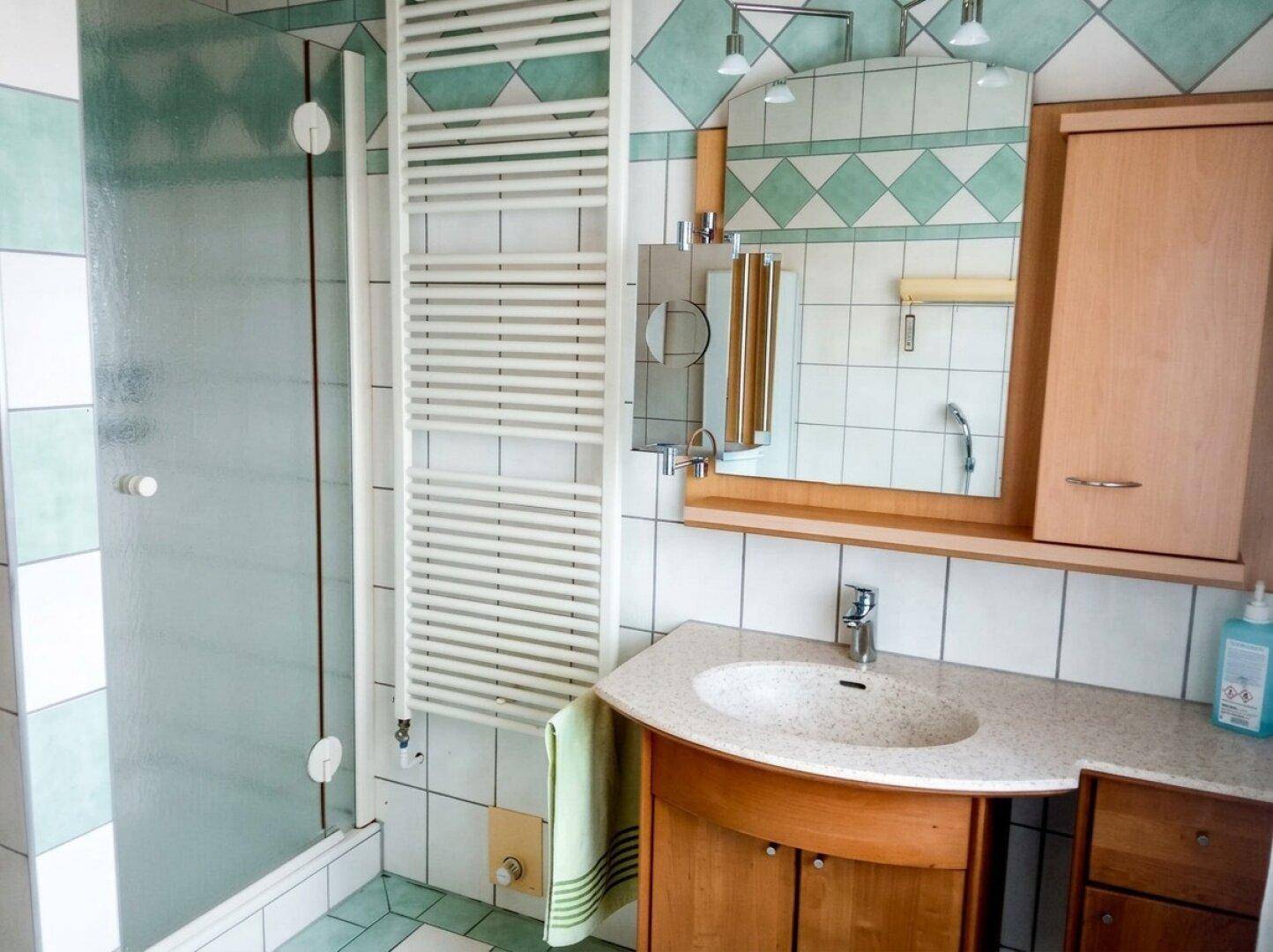 Badezimmer mit Duschkabine, Waschtisch und beheiztem Handtuchhalter.