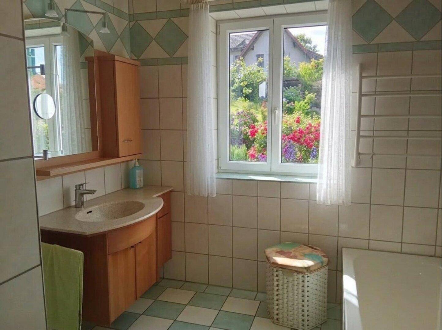 Helles Badezimmer mit Waschtisch, Spiegel und Fenster mit Blick in den Garten.