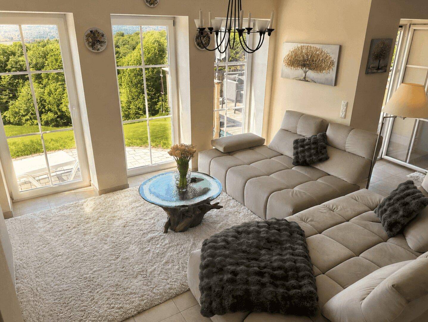 Gemütliches Wohnzimmer mit großem Sofa und weitem Blick ins Grüne durch hohe Fenster.
