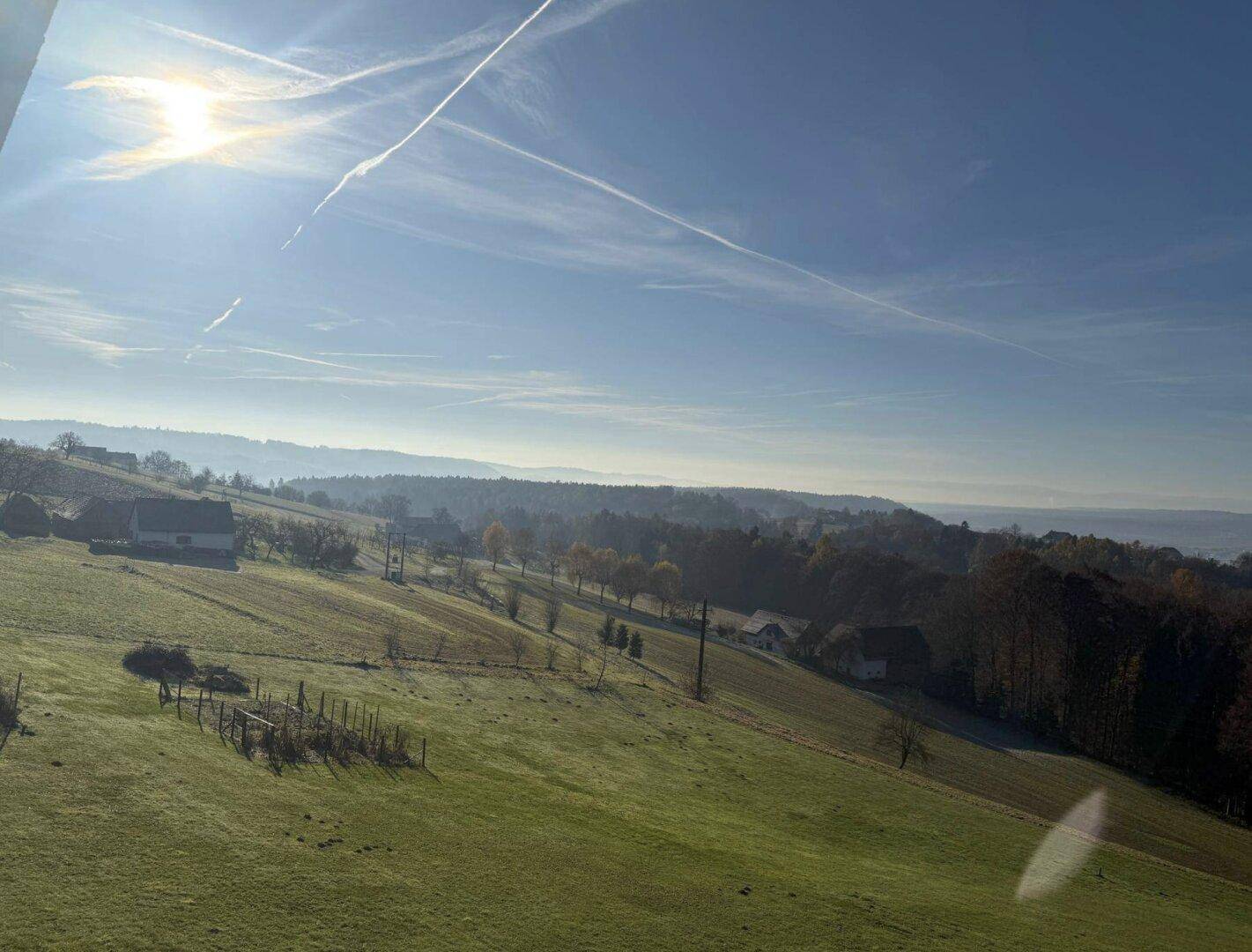 Weitläufige grüne Hügellandschaft mit vereinzelten Häusern unter einem klaren Himmel.