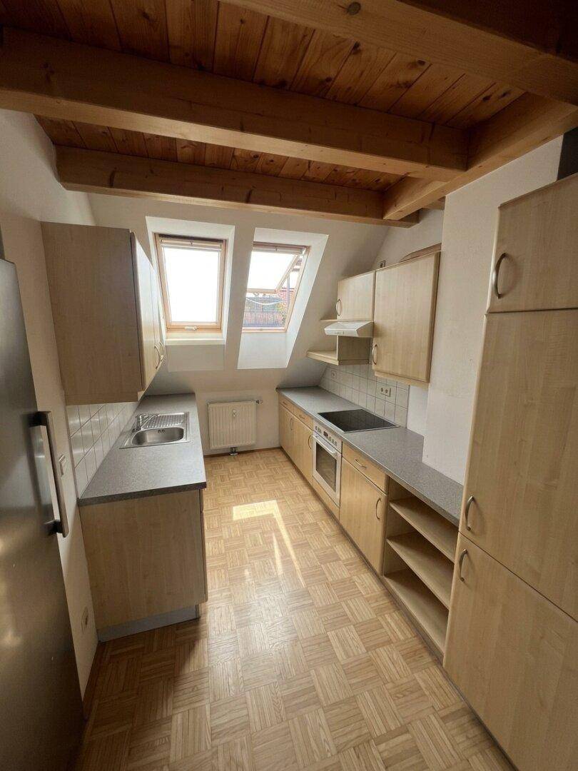Funktionale Küche im Dachgeschoss mit Holzschränken, Parkettboden und zwei Dachfenstern.