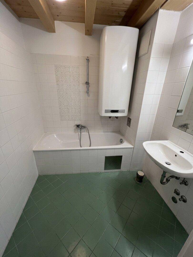 Badezimmer mit Badewanne, Waschbecken, weißen Wandfliesen und grünen Bodenfliesen.