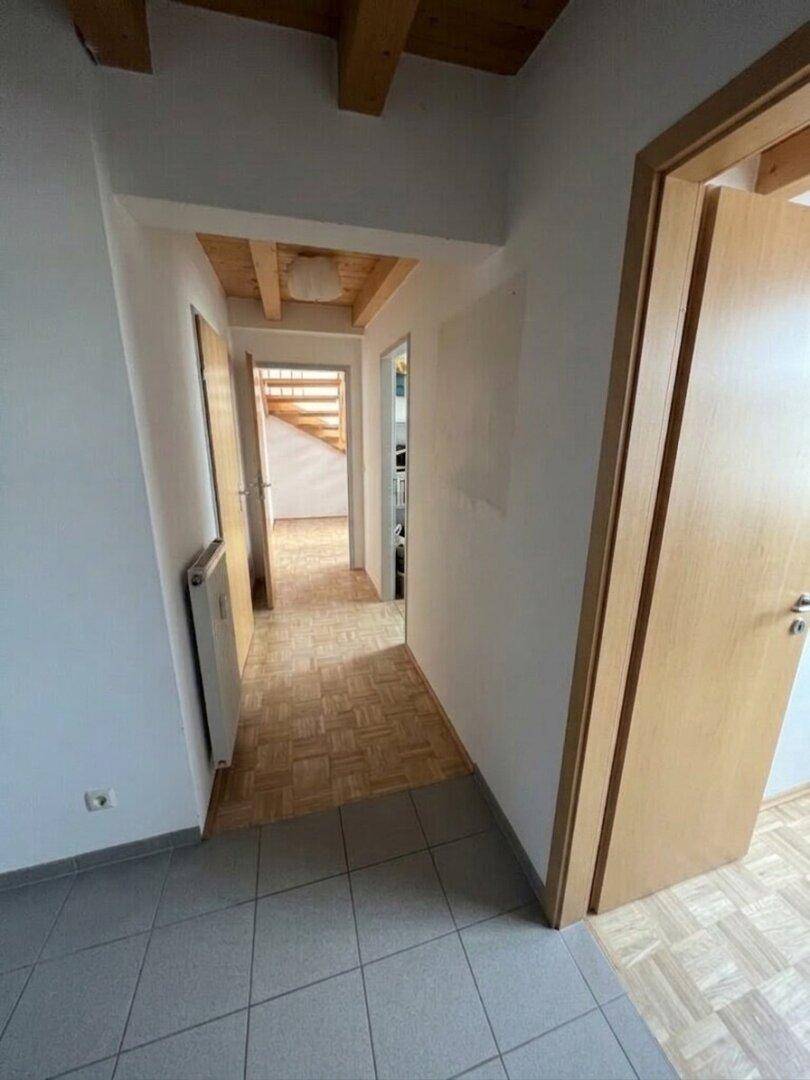 Flur mit Parkett- und Fliesenboden, weißen Wänden und sichtbaren Holzbalken an der Decke.