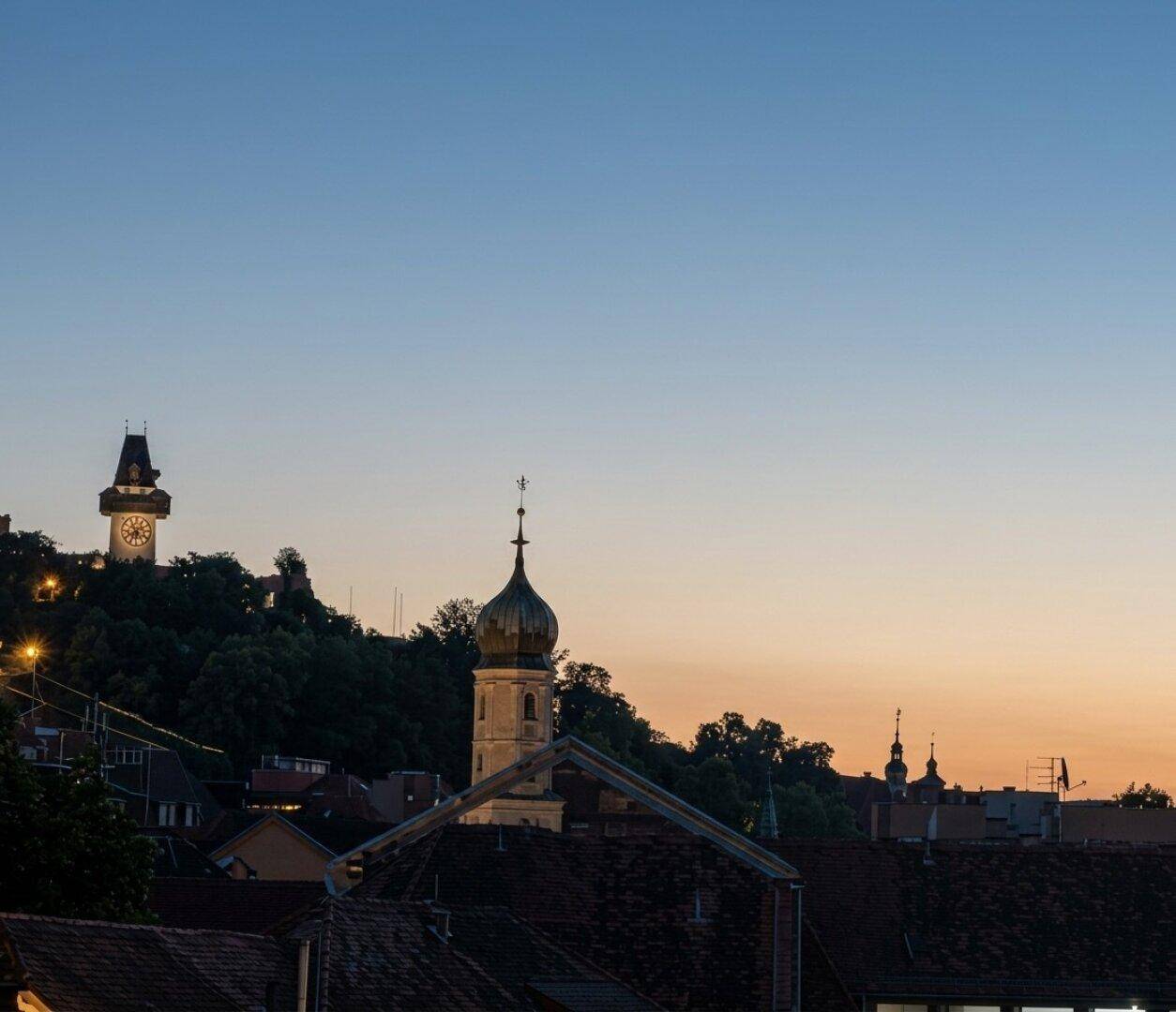 Abendlicher Blick auf die Stadt mit historischen Gebäuden und dem Uhrturm im Hintergrund.