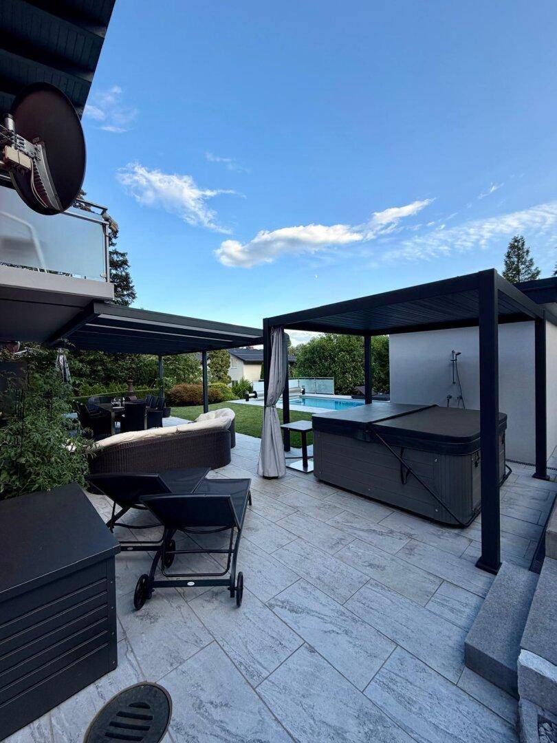 Moderne Terrasse mit Whirlpool unter einer Pergola und gemütlicher Outdoor-Sitzgruppe.