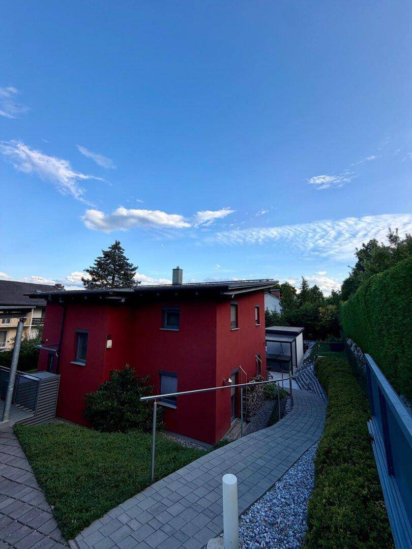 Seitenansicht des roten Hauses mit gepflastertem Weg und grünen Hecken.
