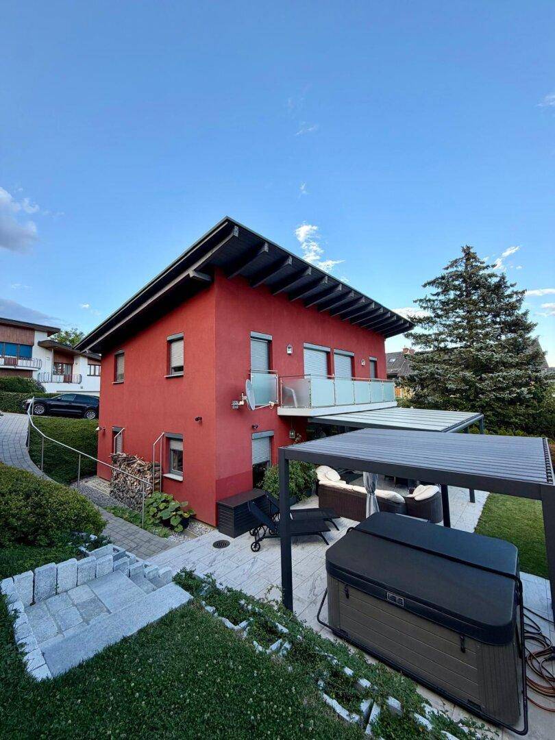 Rotes Haus mit Balkon und einer modernen Terrasse mit Whirlpool und Pergola.