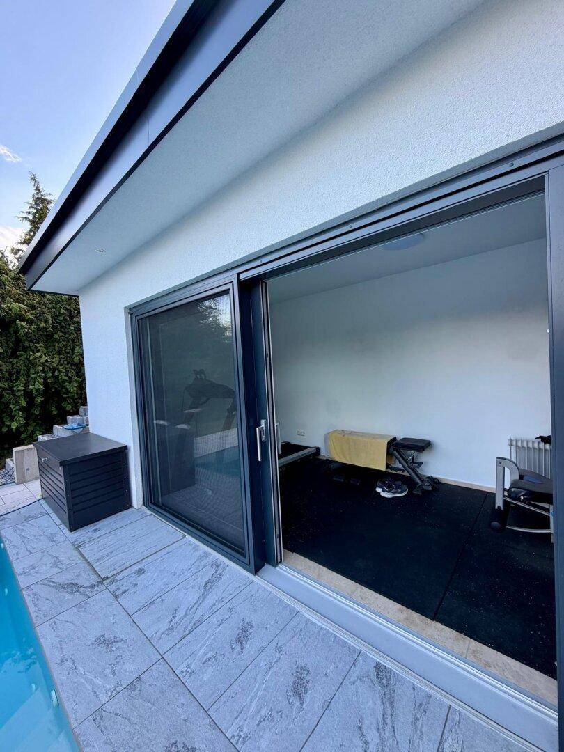 Modernes Poolhaus mit großen Glasschiebetüren, das als Fitnessraum genutzt wird.
