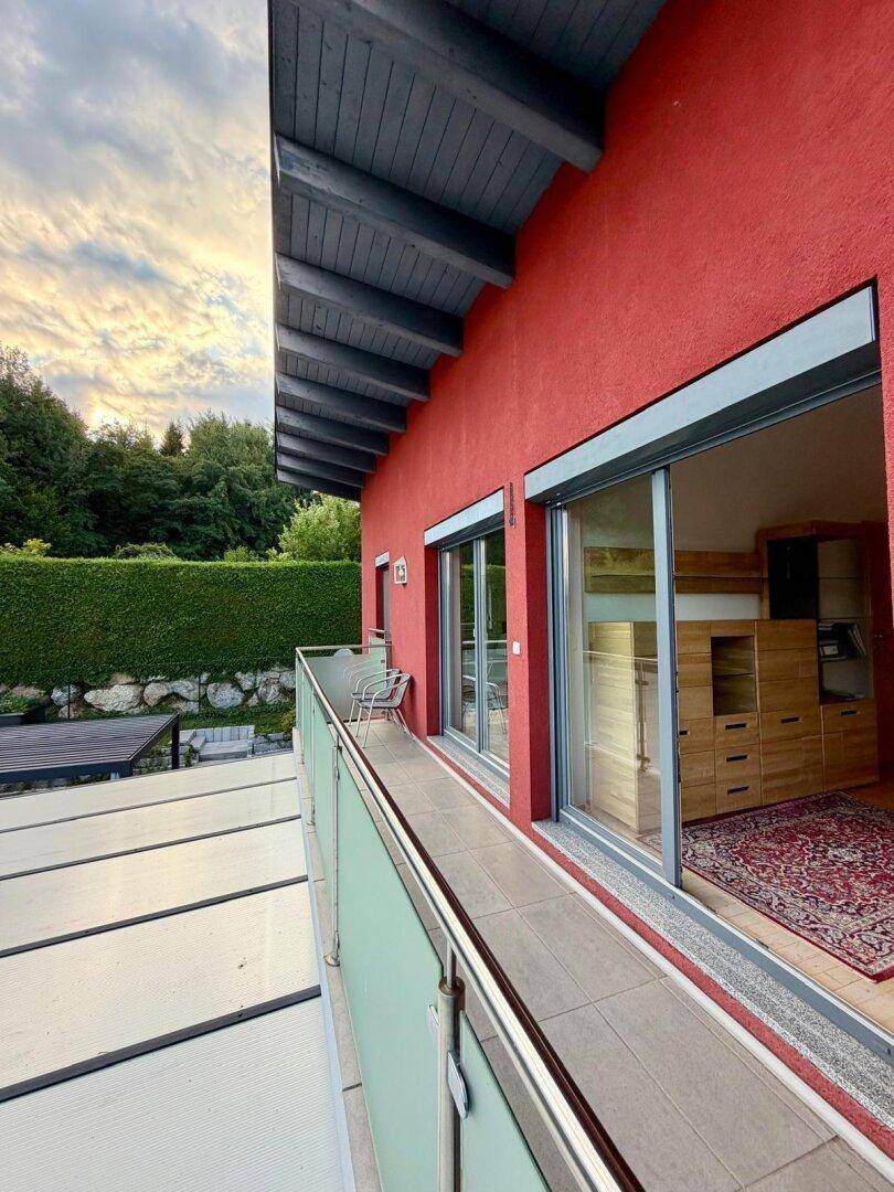 Langer Balkon mit Glasgeländer und Schiebetüren, bietet einen Blick ins Grüne.