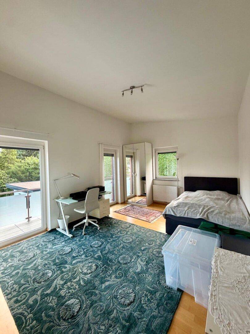 Helles Schlafzimmer mit Holzboden, Schreibtisch und direktem Zugang zu einem Balkon.