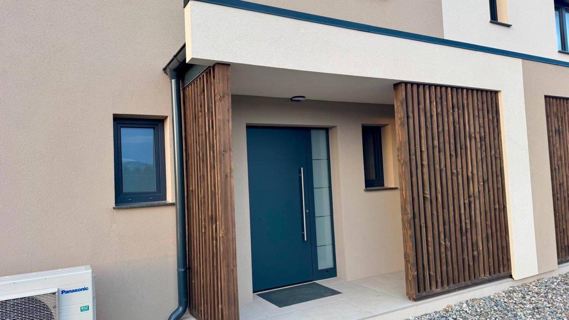 Moderner Hauseingang mit dunkler Tür und vertikalen Holzlamellen an der Fassade.