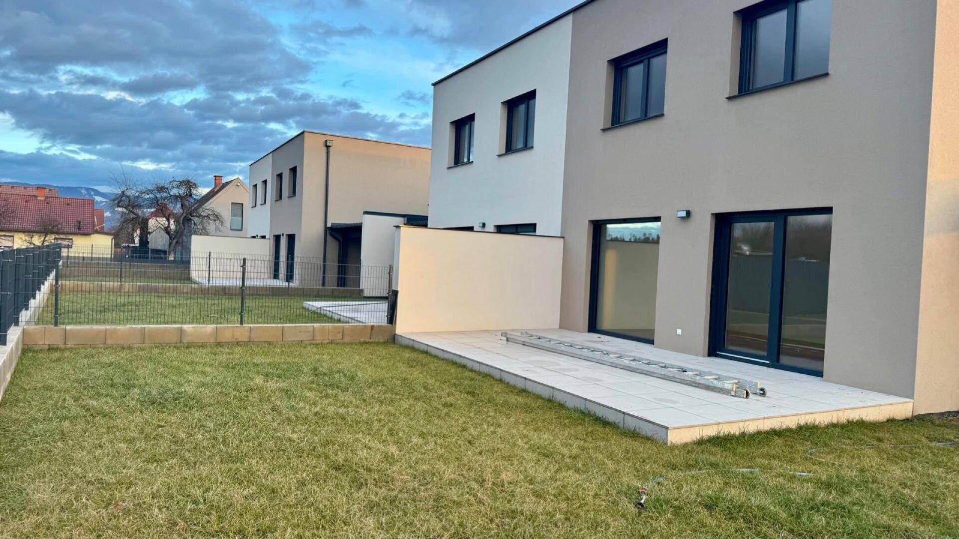 Neuer Gartenbereich mit kleiner gepflasterter Terrasse und Rasenfläche hinter dem Haus.