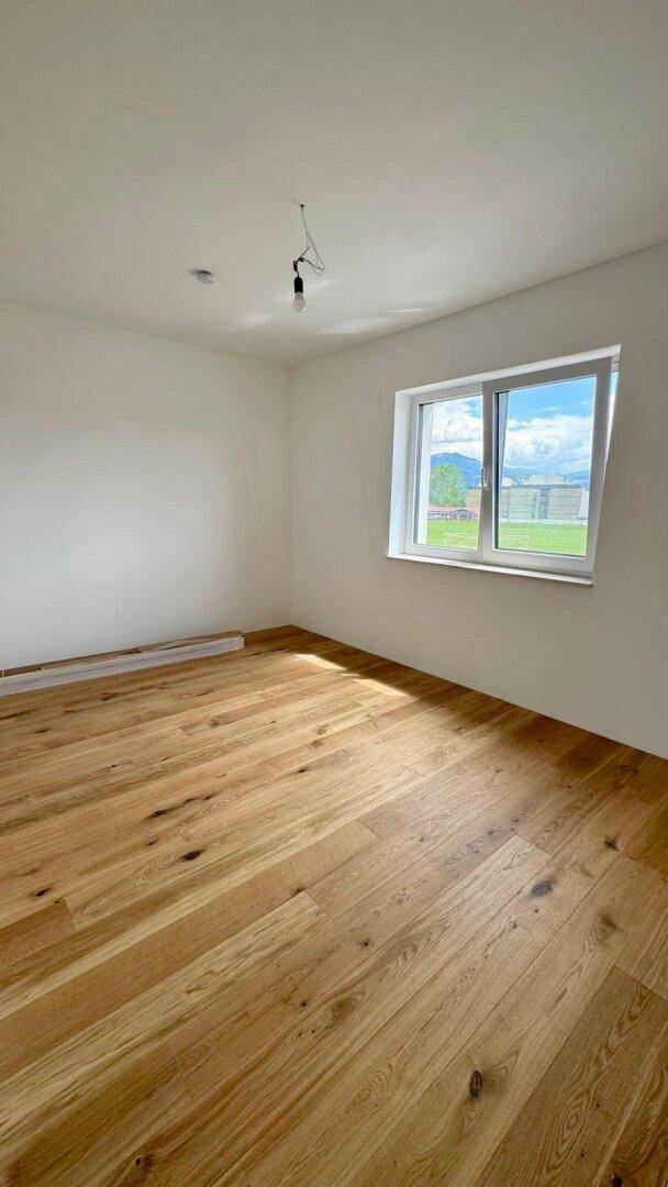 Geräumiges Schlafzimmer mit Holzboden und Fenster, das einen weiten Blick ins Grüne ermöglicht.
