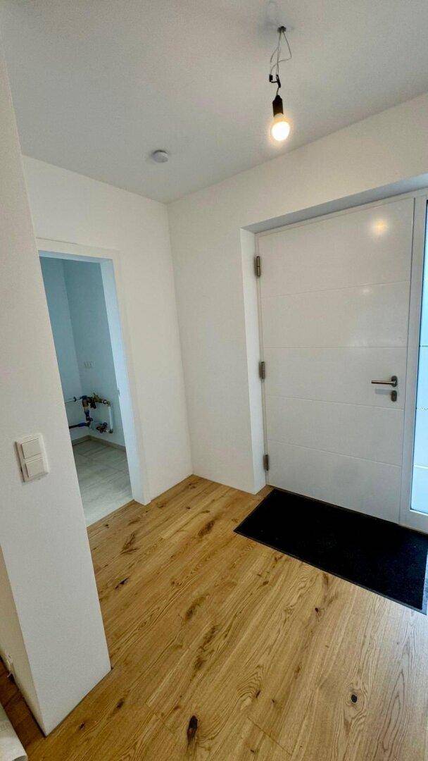 Heller Eingangsbereich mit Holzboden, einer dunklen Fußmatte und einer modernen weißen Tür.