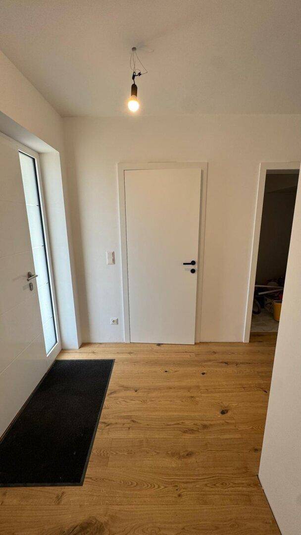 Heller Eingangsbereich mit Holzboden, einer dunklen Fußmatte und einer modernen weißen Tür.