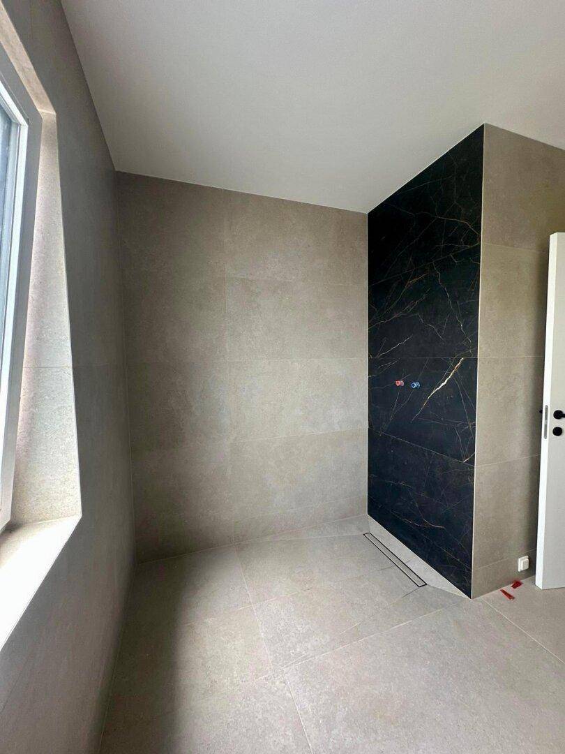Modernes Badezimmer im Bau mit großformatigen Fliesen und einer eleganten Marmorwand in der Dusche.