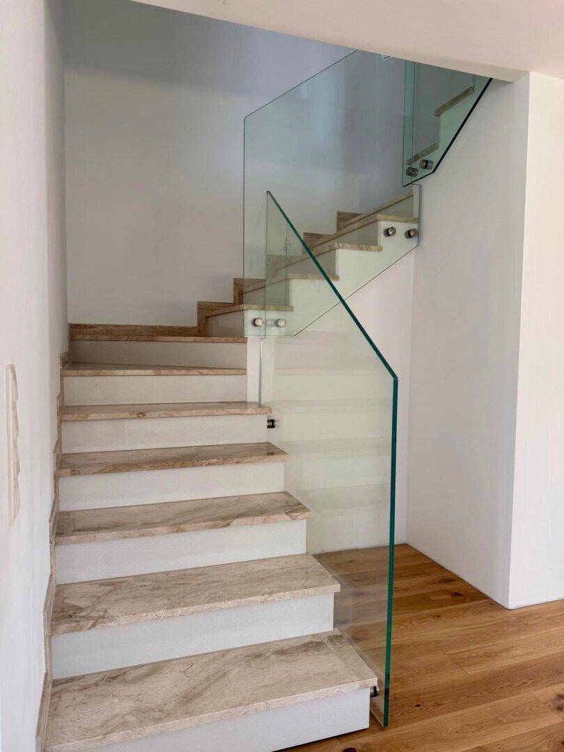 Moderne Treppe mit Natursteinstufen und eleganter Glasbrüstung, die die Etagen verbindet.