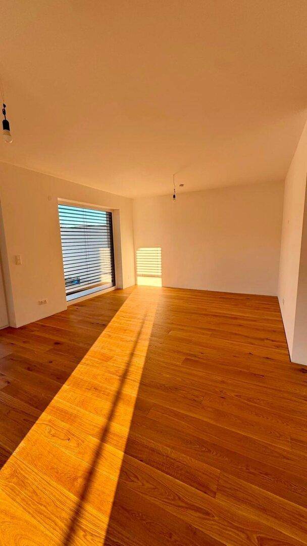Geräumiger, heller Raum mit Holzboden und Fenster, das viel Sonnenlicht hereinlässt.
