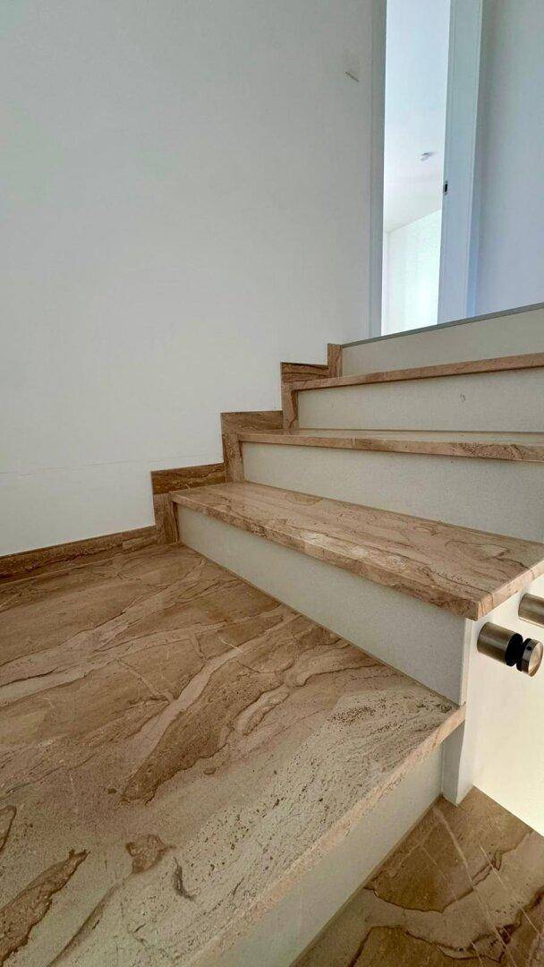 Moderne Treppe mit eleganten Marmorstufen und minimalistischem Design in einem hellen Flur.