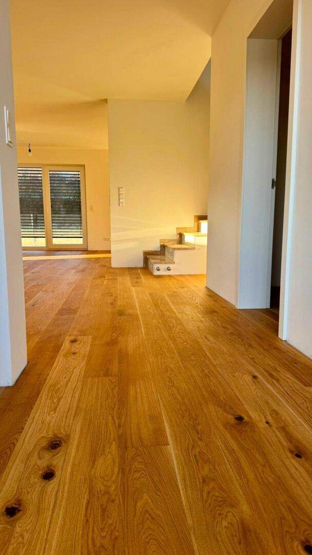 Heller Flur mit durchgehendem Holzboden, der zum Wohnbereich und zur Treppe führt.