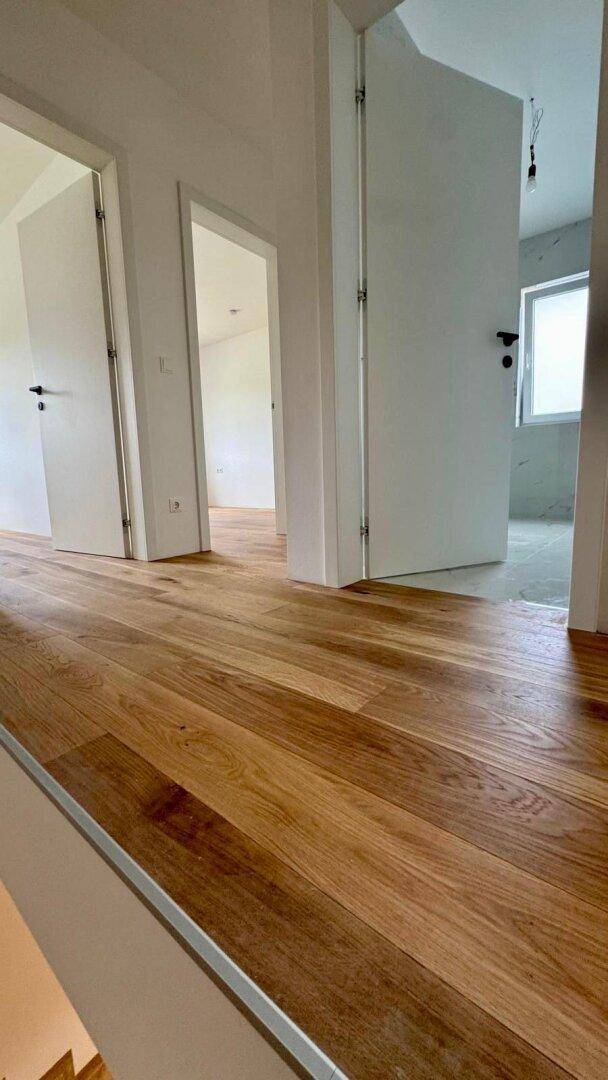 Heller Flur mit Holzboden und mehreren offenen Türen, die zu verschiedenen Räumen führen.