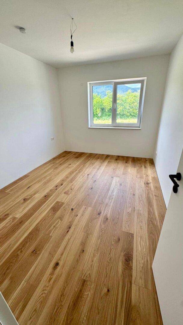 Helles Schlafzimmer mit Holzboden und Fenster, das einen ruhigen Blick ins Grüne bietet.