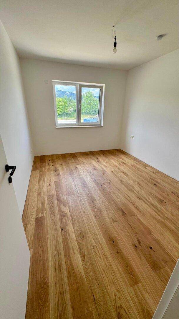 Helles Schlafzimmer mit Holzboden und Fenster, das einen schönen Blick ins Grüne bietet.