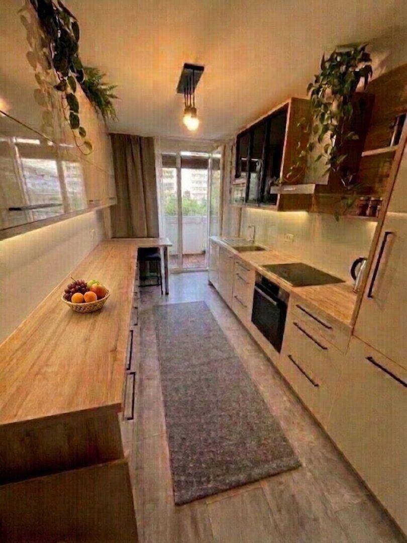 Lange Küche mit Holz-Arbeitsplatten, modernen Schränken und Zugang zum Balkon.