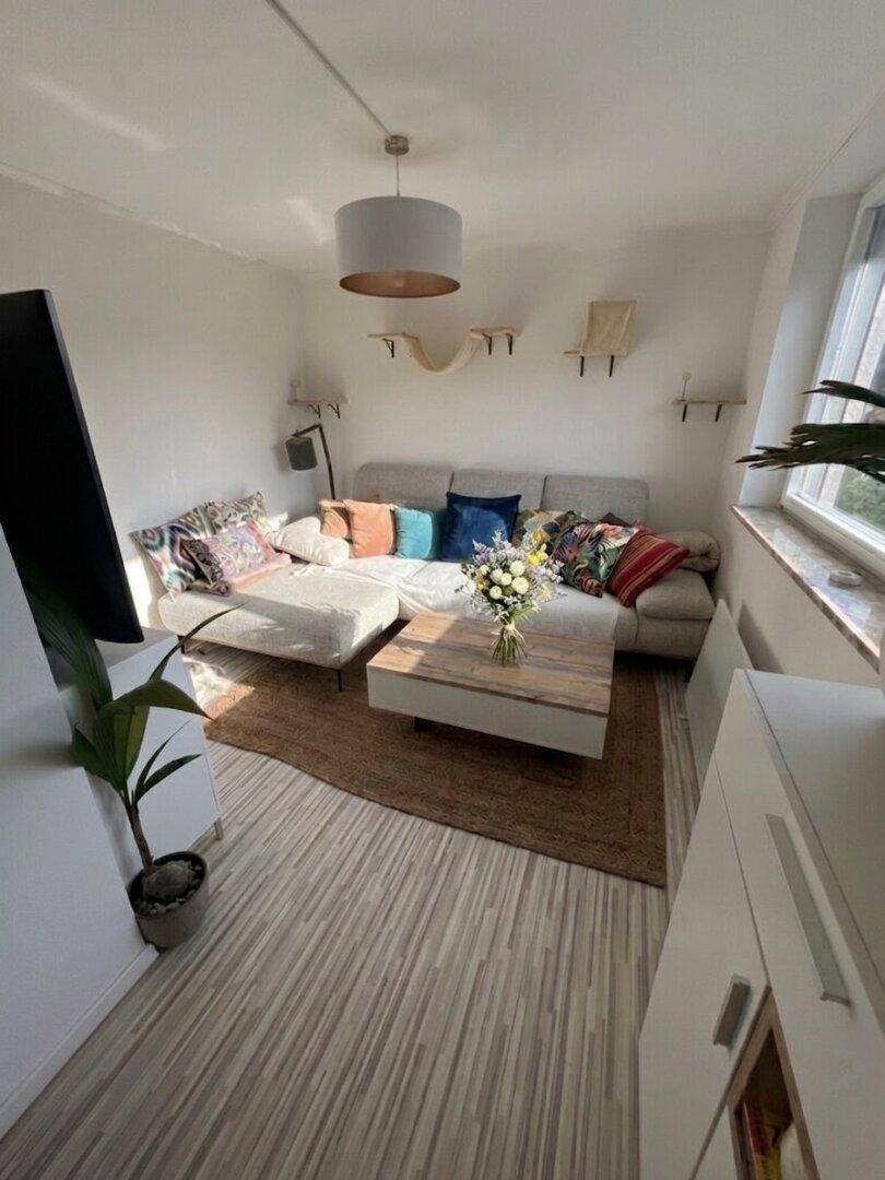 Helles Wohnzimmer mit beigem Ecksofa, Holztisch und Laminatboden.
