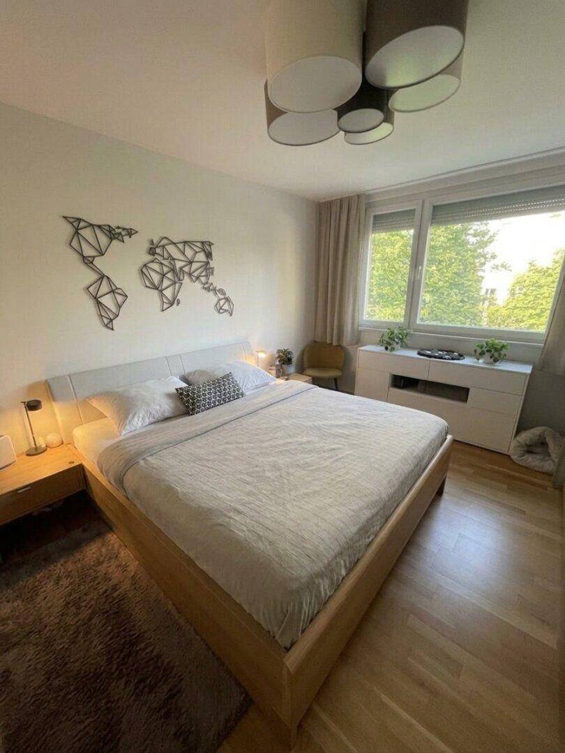 Helles Schlafzimmer mit Doppelbett, Holzboden und Fenster mit Blick ins Grüne.
