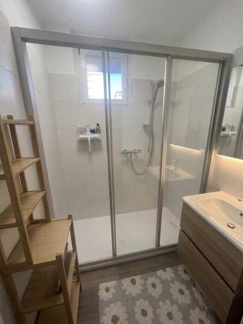 Modernes Badezimmer mit Duschkabine, Waschbecken und hellen Fliesen.