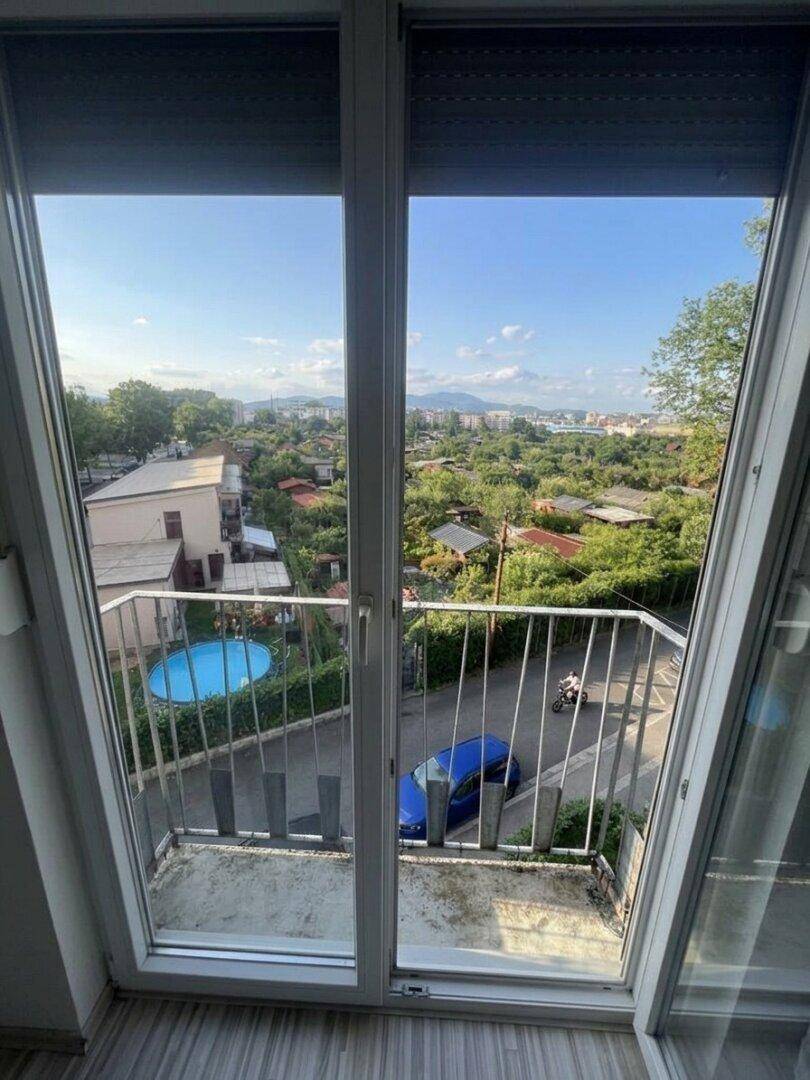 Heller Innenraum mit großem Fenster und Blick auf die umliegende Wohngegend und Berge.