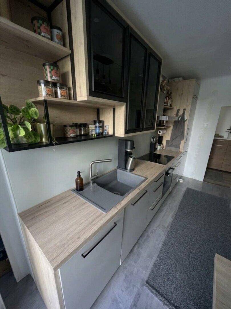 Moderne Küche mit hellen Holzfronten, schwarzen Akzenten und integrierter Spüle.