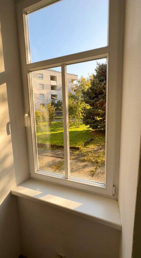 Fenster mit hellem Ausblick ins Grüne und auf umliegende Wohngebäude.