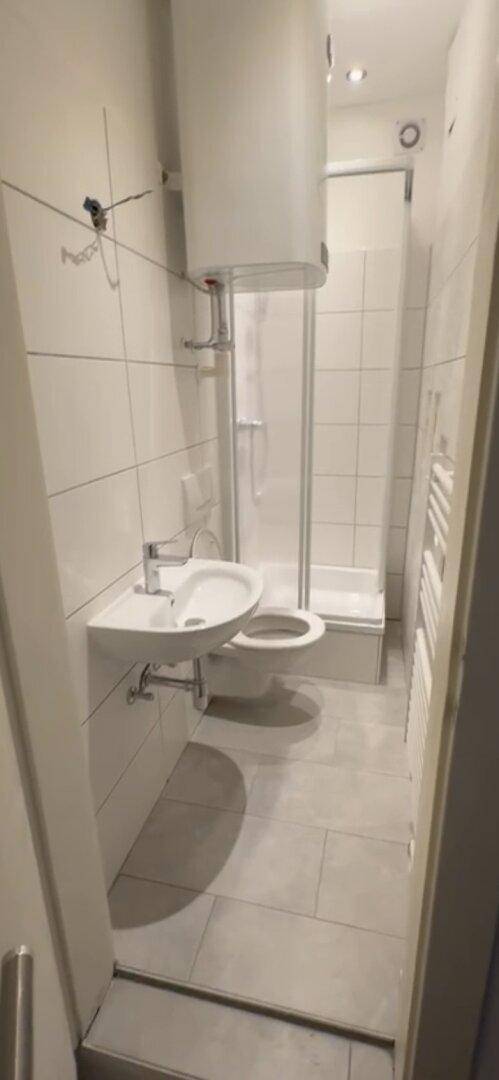 Kleines Badezimmer mit Dusche, WC, Waschbecken und weißen Wand- und Bodenfliesen.