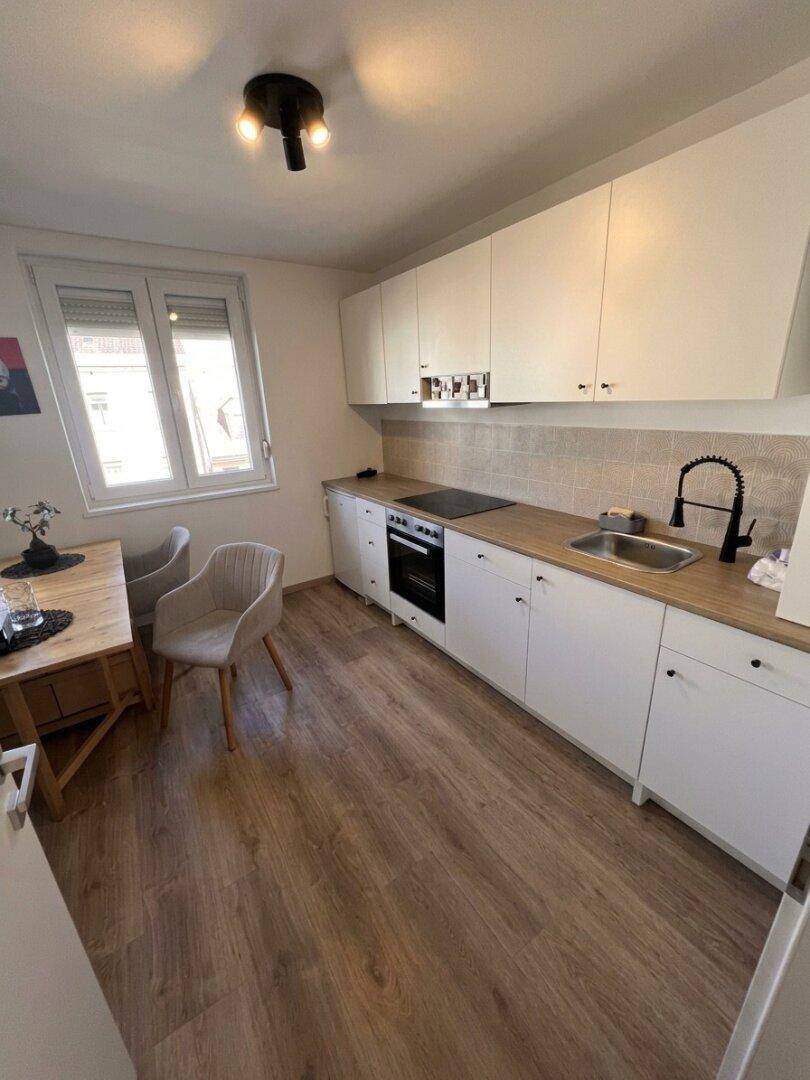 Helle, moderne Küche mit Holzarbeitsplatte, Induktionskochfeld und Essbereich am Fenster.