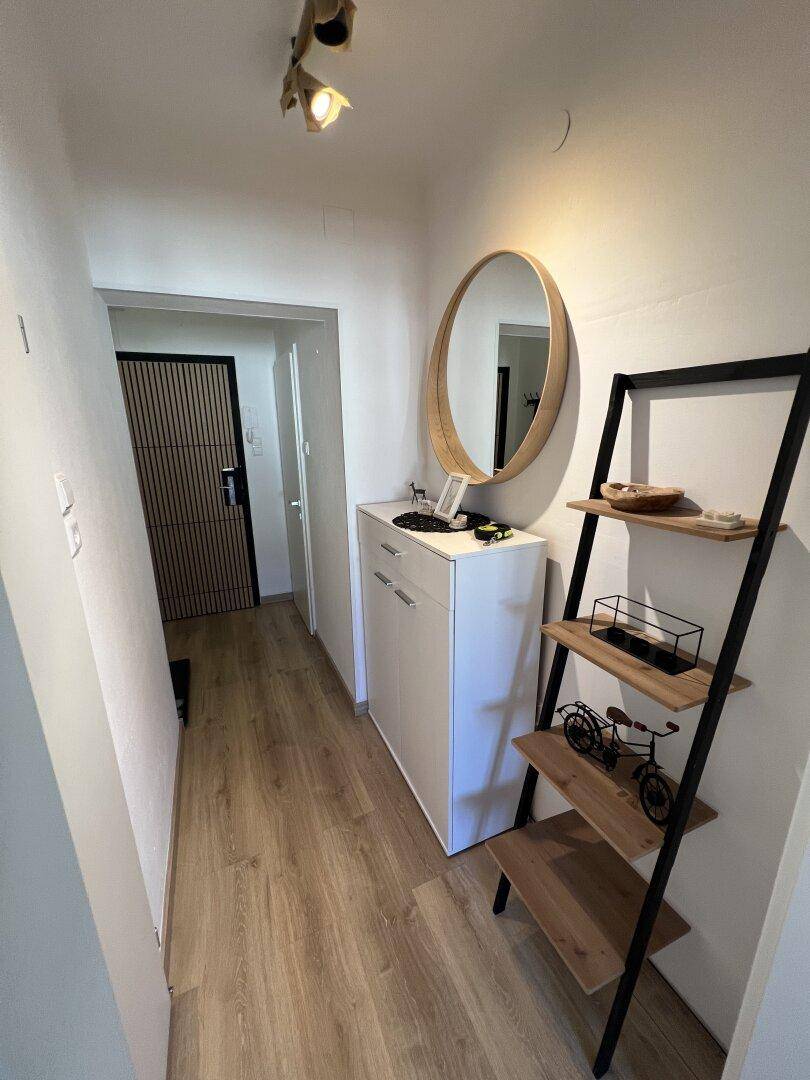 Heller Flur mit Laminatboden, Spiegel und modernem Regal.
