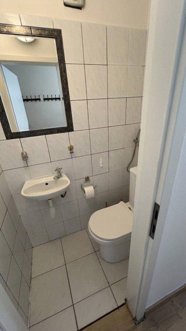 Kleines Gäste-WC mit weißen Fliesen, Wand-WC und Handwaschbecken.