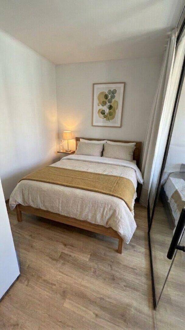 Helles Schlafzimmer mit Doppelbett, Nachttischlampe und modernem Kunstwerk.