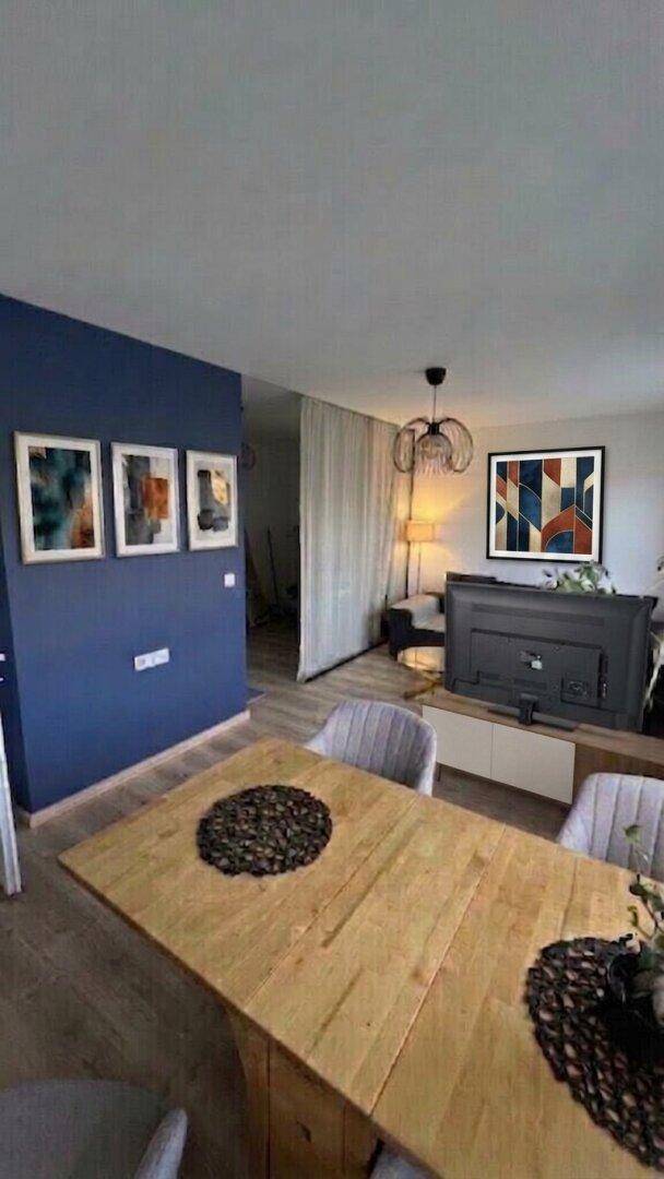 Essbereich mit Holztisch und Stühlen, angrenzend an den Wohnbereich mit blauer Wand.