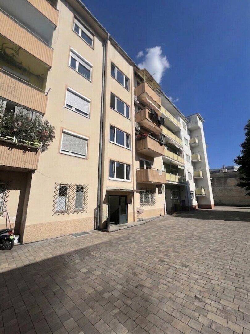 Außenansicht eines Mehrfamilienhauses mit Balkonen und gepflastertem Vorplatz.