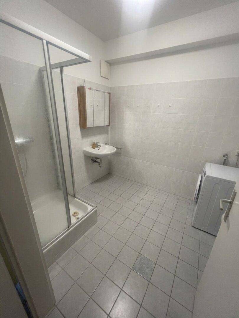 Badezimmer mit Duschkabine, Waschbecken und Waschmaschine, komplett gefliest für einfache Pflege.