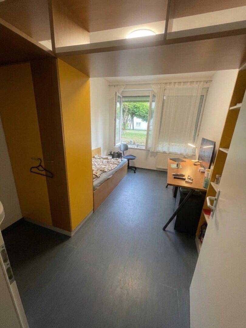 Kleines Schlafzimmer mit Einzelbett, Schreibtisch und integriertem Kleiderschrank, ideal für Studenten.