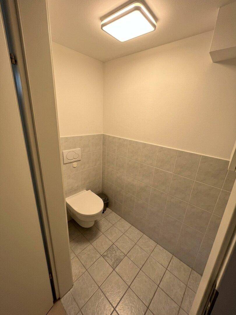 Separates WC mit wandhängender Toilette und hellen Fliesen, praktisch und platzsparend.
