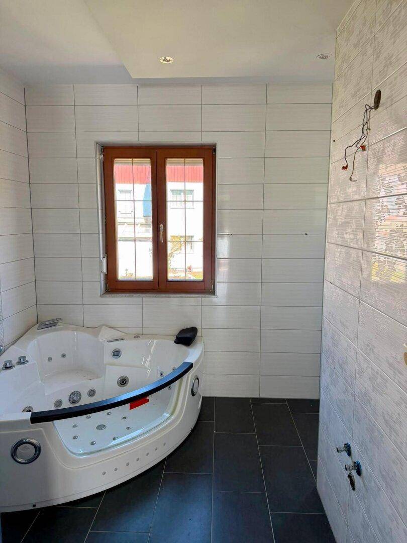 Helles Badezimmer mit Eck-Whirlpoolwanne und einem Fenster für natürliches Tageslicht.
