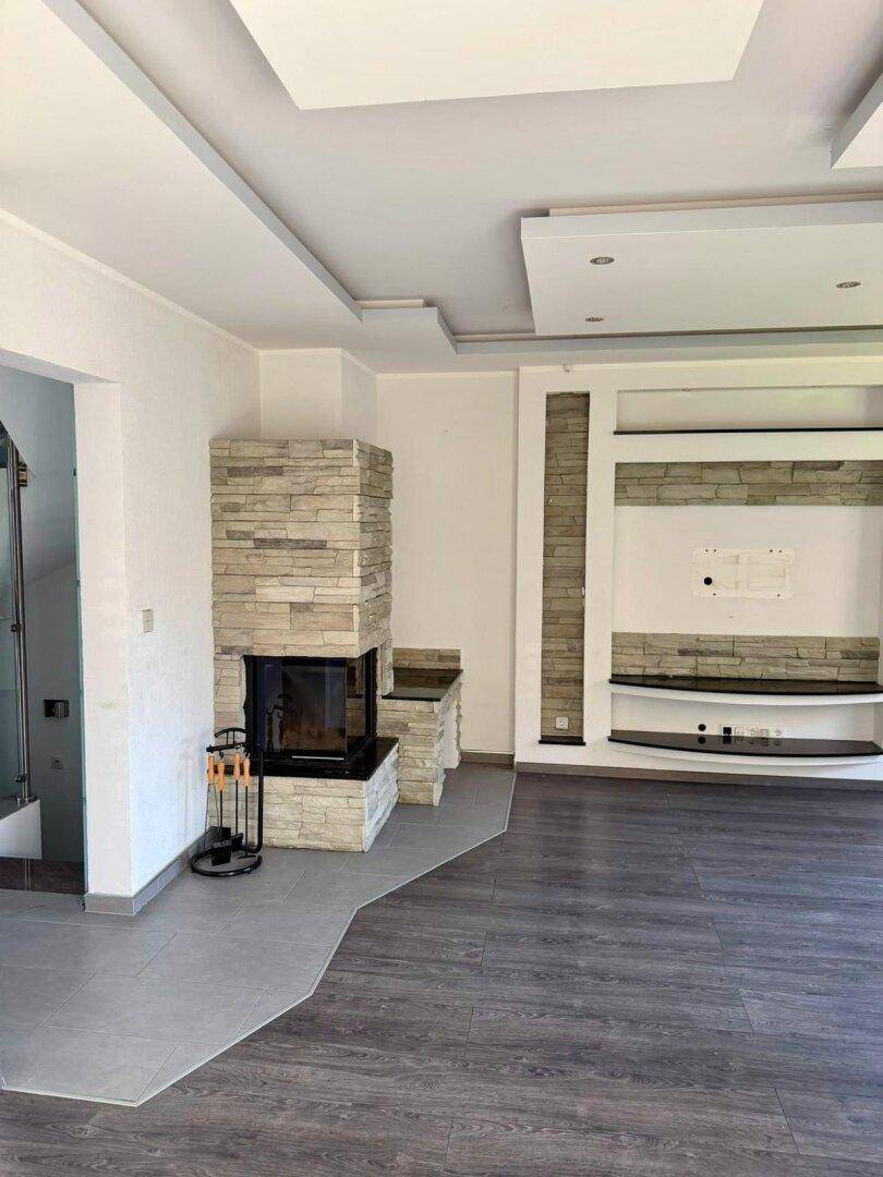 Geräumiges Wohnzimmer mit modernem Kamin und stilvoller Wandgestaltung in hellen Tönen.